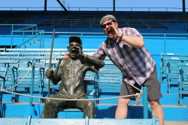 Coach Tom Simon poses with a statue honoring a fan who attended every game for many years at the Estadio Latinoamericano.